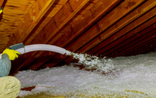 Technician Spraying Blown Fiberglass Insulation Between Attic Tr